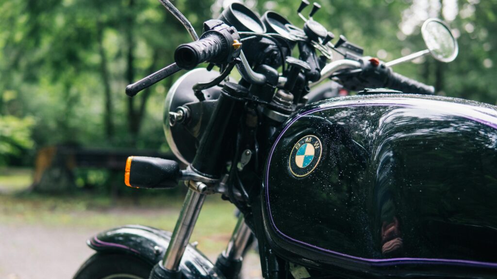 Close-up of a classic motorcycle with raindrops on a forest road, showcasing elegant retro design.